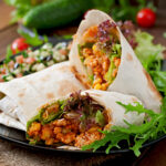 Burritos wraps with minced beef and vegetables on a wooden background