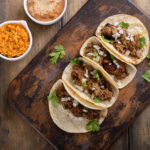 Pork carnitas tacos with onion and cilantro served with Mexican rice and refried beans