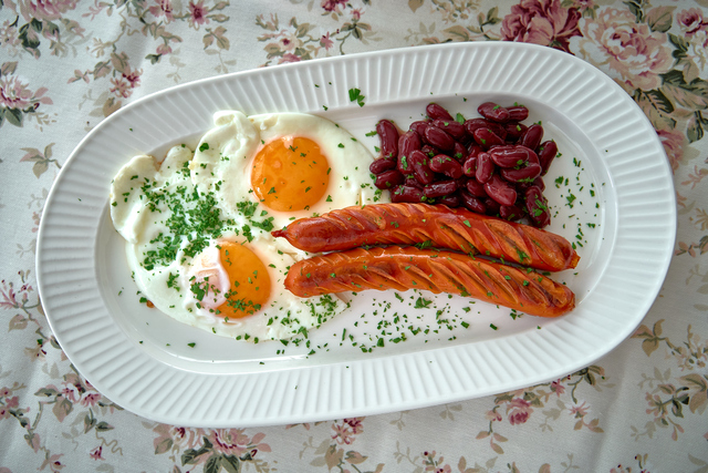 A Delicious Breakfast Plate Featuring Sunny-Side Up Eggs, Tasty Sausages, and Flavorful Red Kidney Beans Accompanied by Fresh Herbs