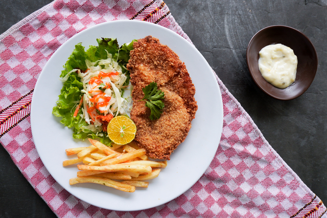 Chicken schnitzel is made from chicken breast, served with French fries, lemon, vegetable salad and sauce, mayonnaise on plate. flat lay