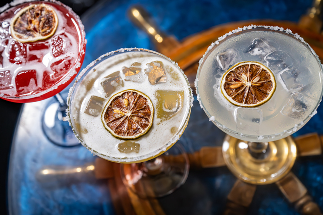 Colorful cocktails served elegantly on a bar table. Three vibrant cocktails sit on a stylish bar table, each garnished with dried lime and surrounded by ice cubes.