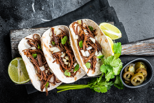 Pork carnitas tacos on corn tortillas with onion and lime. Black background. Top view